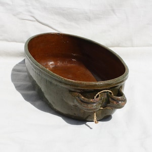 Puede incluir: Un plato de servir ovalado de cerámica verde glaseado con dos asas. El interior del plato es de color marrón rojizo.