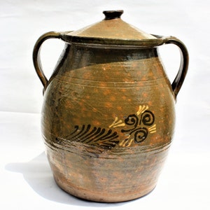 May include: A large, brown earthenware crock with a lid and two handles. The crock has a decorative design painted in black and gold.