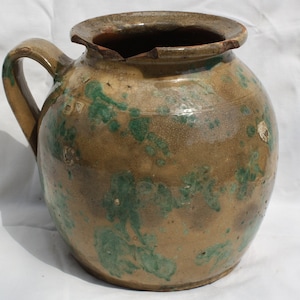May include: A large, round, brown ceramic pitcher with a green glaze. The pitcher has a handle and a wide mouth.