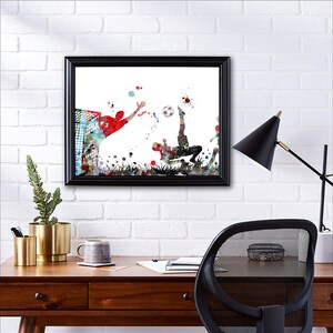 Puede incluir: Pintura acuarela de dos jugadores de f&uacute;tbol en acci&oacute;n. Un jugador est&aacute; pateando el bal&oacute;n mientras que el otro jugador se lanza para salvarlo. La pintura est&aacute; enmarcada en negro.