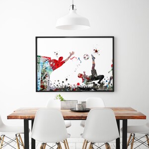 Puede incluir: Una pintura de acuarela de dos jugadores de f&uacute;tbol en acci&oacute;n. Un jugador est&aacute; pateando el bal&oacute;n mientras que el otro jugador lo est&aacute; alcanzando. La pintura est&aacute; en un marco negro y est&aacute; colgada en una pared blanca.