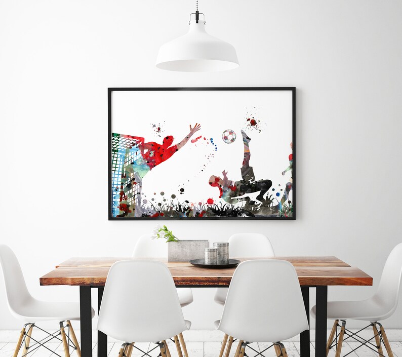 Puede incluir: Una pintura de acuarela de dos jugadores de f&uacute;tbol en acci&oacute;n. Un jugador est&aacute; pateando el bal&oacute;n mientras que el otro jugador lo est&aacute; alcanzando. La pintura est&aacute; en un marco negro y est&aacute; colgada en una pared blanca.