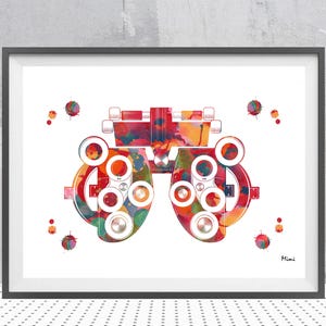 May include: Watercolor print of an eye exam phoropter in a black frame. The phoropter is depicted in vibrant colors of red, orange, yellow, green, and blue. The print includes small paint splatters and the artist's signature.