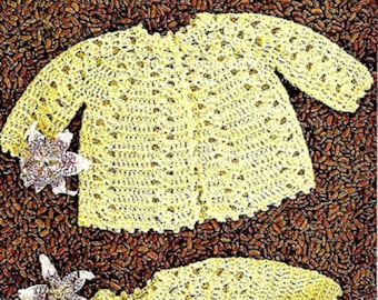 May include: Two crocheted baby sweaters in a pale yellow color, laid out on a brown background. The sweaters have a delicate lace pattern and are perfect for a newborn.