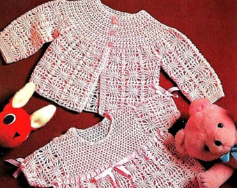 May include: A white crocheted baby dress and cardigan set with pink ribbon accents. The dress has a round neckline and short sleeves. The cardigan has a button closure and long sleeves.