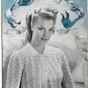 May include: A white crocheted bed jacket with a delicate lace pattern. The jacket has a collar and buttons down the front. The model is wearing the jacket and holding a book.