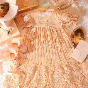 May include: A crocheted baby dress with a scalloped hem and matching bonnet. The dress is made in a delicate peach color and features a delicate floral pattern.