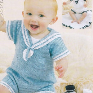 May include: A blue knitted baby outfit with white trim, featuring a sailor collar and short sleeves. The outfit is worn by a baby sitting on a fuzzy surface. The image also shows a pair of white and blue knitted baby booties.
