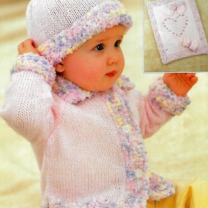 Op de afbeelding: Een roze gebreid babyvestje met een witte en roze rand. Het vestje heeft een klein hartvormig ontwerp aan de voorkant. De baby draagt een bijpassende roze gebreide muts.