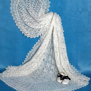 Puede incluir: Una manta de bebé de ganchillo blanco con un delicado patrón de encaje. La manta está drapeada sobre una superficie azul y tiene un borde festoneado.