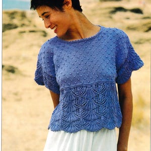 May include: A blue knitted top with short sleeves. The top has a textured pattern on the upper section and a scalloped design on the lower section. The words "DOUBLE KNITTING" are in the upper left corner.
