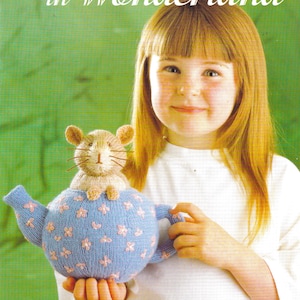 May include: A knitted toy featuring a light brown dormouse emerging from a light blue teapot decorated with small pink floral patterns. The text Alice in Wonderland is printed at the top, and Dormouse in Teapot Toy is printed at the bottom.