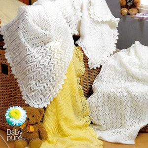 Puede incluir: Tres mantas de bebé de ganchillo blanco con delicados bordes de encaje, una manta de bebé de ganchillo amarilla y un oso de peluche marrón. Las mantas se muestran en una cesta de mimbre.