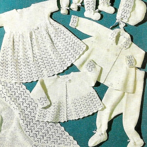 Puede incluir: Un conjunto de ropa de bebé de punto blanco que incluye un vestido, un cárdigan, pantalones, botines y un gorro. El conjunto está hecho con un delicado patrón de encaje.