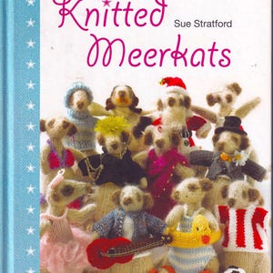 Könnte beinhalten: Das Buchcover "Knitted Meerkats" von Sue Stratford. Es zeigt eine Gruppe gestrickter Erdmännchen-Figuren, jede mit unterschiedlicher Kleidung, wie einem Weihnachtsmannhut, einem Smoking und einem gestreiften Oberteil. Der Hintergrund ist weiß mit einem blauen Streifen und Sternmuster.