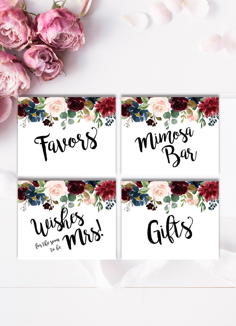 May include: Four white signs with floral borders in shades of burgundy, pink, and blue. The signs read "Favors", "Mimosa Bar", "Wishes for the soon to be Mrs.", and "Gifts".
