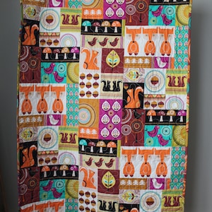 May include: A patchwork quilt with a woodland theme. The quilt features a variety of animals, including foxes, squirrels, and birds. The quilt is made up of different colored squares, including brown, orange, green, and blue.