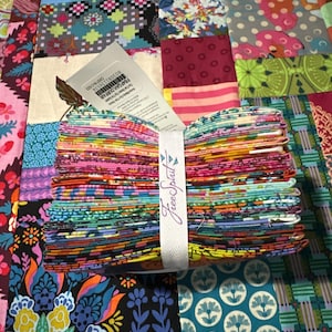 May include: A stack of folded fabric squares held together by a white paper band labeled FreeSpirit. The fabric features a variety of colorful patterns including butterflies, floral motifs, geometric shapes, and stripes in shades of pink, blue, yellow, and green.