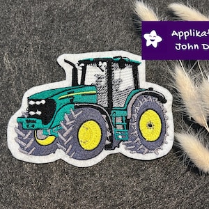 Könnte beinhalten: Gestickter Aufnäher eines grünen und gelben John Deere Traktors. Der Traktor hat schwarze Reifen und eine weiße Umrandung. Der Aufnäher hat den Text "Applikation John Deere" auf lila Hintergrund.