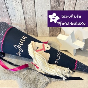 Könnte beinhalten: Ein schwarzer Schultüte mit einem weißen Pferde-Applique, einem rosa Band und dem Namen "Juna" bestickt. Die Schultüte hat außerdem einen weißen Punktensaum und das Datum "09.2021" bestickt. Die Schultüte liegt auf einem weißen Fell. Der Text "Schultüte Pferd Galaxy" ist in der oberen rechten Ecke des Bildes zu sehen.