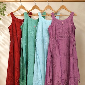 May include: Four sleeveless dresses hanging on wooden hangers, each featuring a scoop neckline and intricate tonal floral embroidery. The dresses are displayed in a row in shades of deep red, sage green, light blue, and purple, all with a tie-waist.