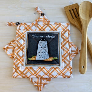 May include: Orange and white quilted pot holder with a grater and carrots design. The text "Carottes râpées" is embroidered on the pot holder.