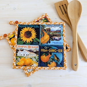 Peut inclure: Ensemble de quatre dessous de plat carrés matelassés avec des motifs d'étiquettes de caisses de fruits vintage. Les dessous de plat présentent des images de tournesol, d'oranges et de paysage. Deux ustensiles de cuisine en bois sont à côté.