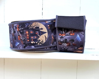 May include: A roll of fabric ribbon featuring a Halloween-themed print with a dark haunted house, a large yellow full moon, glowing orange pumpkins, and white ghosts against a dark purple and black background, finished with a black velcro strap.