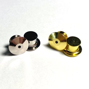 May include: Two sets of metal pin backs, one set is silver and the other is gold. Each set has two pin backs.