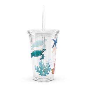 May include: A clear plastic tumbler with a lid and straw. The tumbler has a design of sea turtles, starfish, and coral.