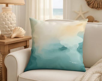 May include: Square cushion featuring an abstract watercolour design in teal, white, and yellow hues. The cushion is placed on a white armchair, suitable for coastal or beach-themed interiors.