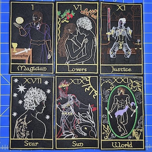 May include: Set of six embroidered tarot card patches on black fabric. Each patch features a different card from the Major Arcana, including The Magician, The Lovers, Justice, The Star, The Sun, and The World. The designs are outlined in gold thread.