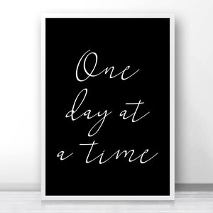 May include: Black and white printable wall art with the text "One day at a time" in a cursive font.