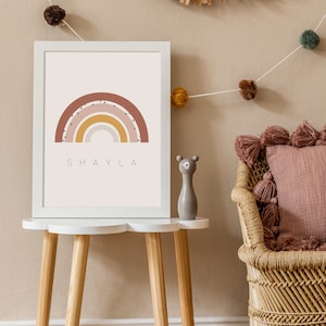 May include: A white framed print with a rainbow design in shades of pink, yellow, and orange. The rainbow has white polka dots and the name "SHAYLA" is printed below it.