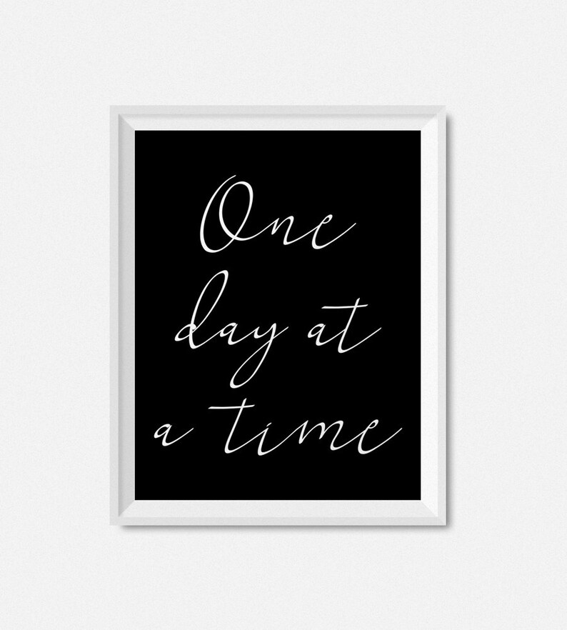 May include: Black and white framed print with the text "One day at a time" in white cursive script.