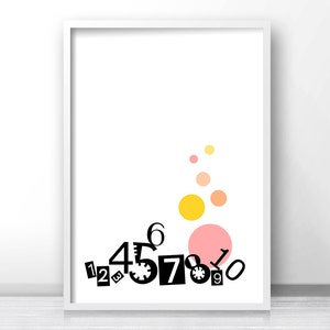 May include: A white framed print with black numbers 1 through 9 scattered across the bottom. The numbers are in a playful, jumbled arrangement. Above the numbers are five colorful circles in shades of pink, orange, and yellow.
