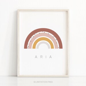 May include: A framed print with a rainbow design in shades of brown, pink, yellow, and gray. The rainbow has white polka dots. The name "ARIA" is printed below the rainbow.