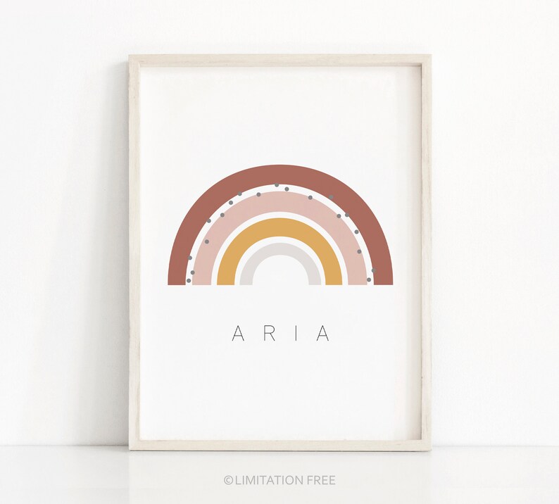 May include: A framed print with a rainbow design in shades of brown, pink, yellow, and gray. The rainbow has white polka dots. The name "ARIA" is printed below the rainbow.