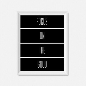 Op de afbeelding: Zwart-wit ingelijste print met de tekst "FOCUS ON THE GOOD" in een wit sans-serif lettertype.
