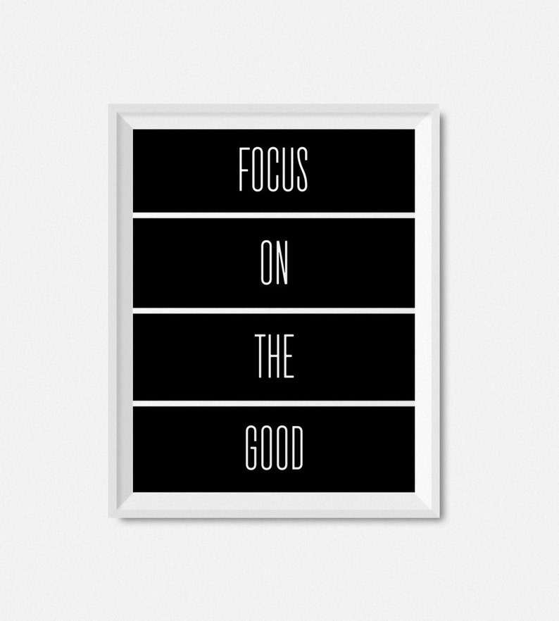 Op de afbeelding: Zwart-wit ingelijste print met de tekst "FOCUS ON THE GOOD" in een wit sans-serif lettertype.