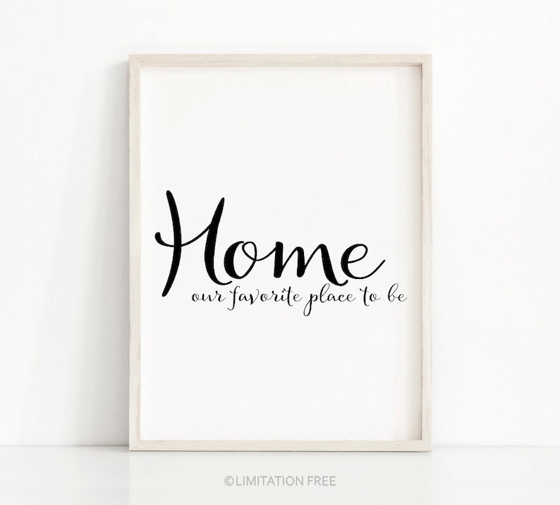 May include: A framed print with the word "Home" in a stylish black script, with the phrase "our favorite place to be" beneath it. The frame is a light wood color, and the background is white.