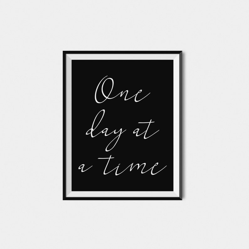 May include: Black and white framed print with the text "One day at a time" in white cursive font on a black background.