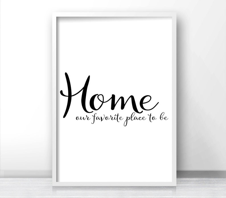 May include: A framed white print with the word "Home" in a stylish black script font. Below, the phrase "our favorite place to be" is written in a smaller, cursive font. The print is displayed against a white background.