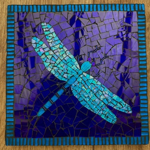 May include: A mosaic artwork of a dragonfly with blue and purple glass tiles. The dragonfly is in flight with its wings spread out.