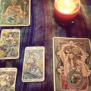 May include: Tarot cards spread out on a table with a lit candle in the background. The cards are from the Rider-Waite deck and include the Eight of Swords, Queen of Wands, and the Aries card.