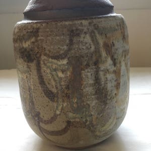 May include: A brown ceramic vase with a mottled glaze in shades of brown, white, and blue. The vase has a rounded shape and a slightly flared lip.