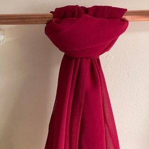 May include: A deep red chiffon scarf draped over a copper pipe rack. The scarf is soft and flowing, with a subtle sheen.