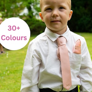 May include: A young boy wearing a white shirt and a pink tie. The tie has a small pocket square with the words "Proud Boy" embroidered on it. The boy is standing in a grassy area. A text overlay says "30+ Colours".