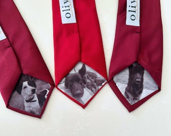 May include: Three red neckties with dog portraits on the underside. Each tie has a white label with the word "olive" printed on it. The ties are arranged on a white surface.