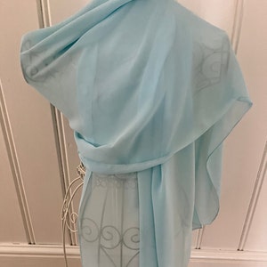 May include: A light blue sheer scarf draped over a mannequin. The scarf is made of a soft, flowing fabric.